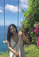 'A sunny outdoor photo of me smiling warmly at the camera. I am wearing a breezy, white sleeveless summer dress with a deep V-neck and subtle gold stripes, paired with a chain-strap crossbody bag. I am standing on green grass next to a rustic rope swing, 