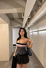 'I am wearing a strapless tube top with pink, white, and black horizontal stripes, paired with a short black skirt. I am holding a dark leather shoulder bag over my arm and carrying a black jacket in my hand.'